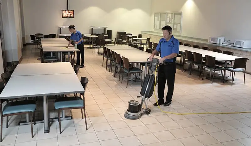 A cleaning crew that is buffering the floor and wiping down tables in a lobby