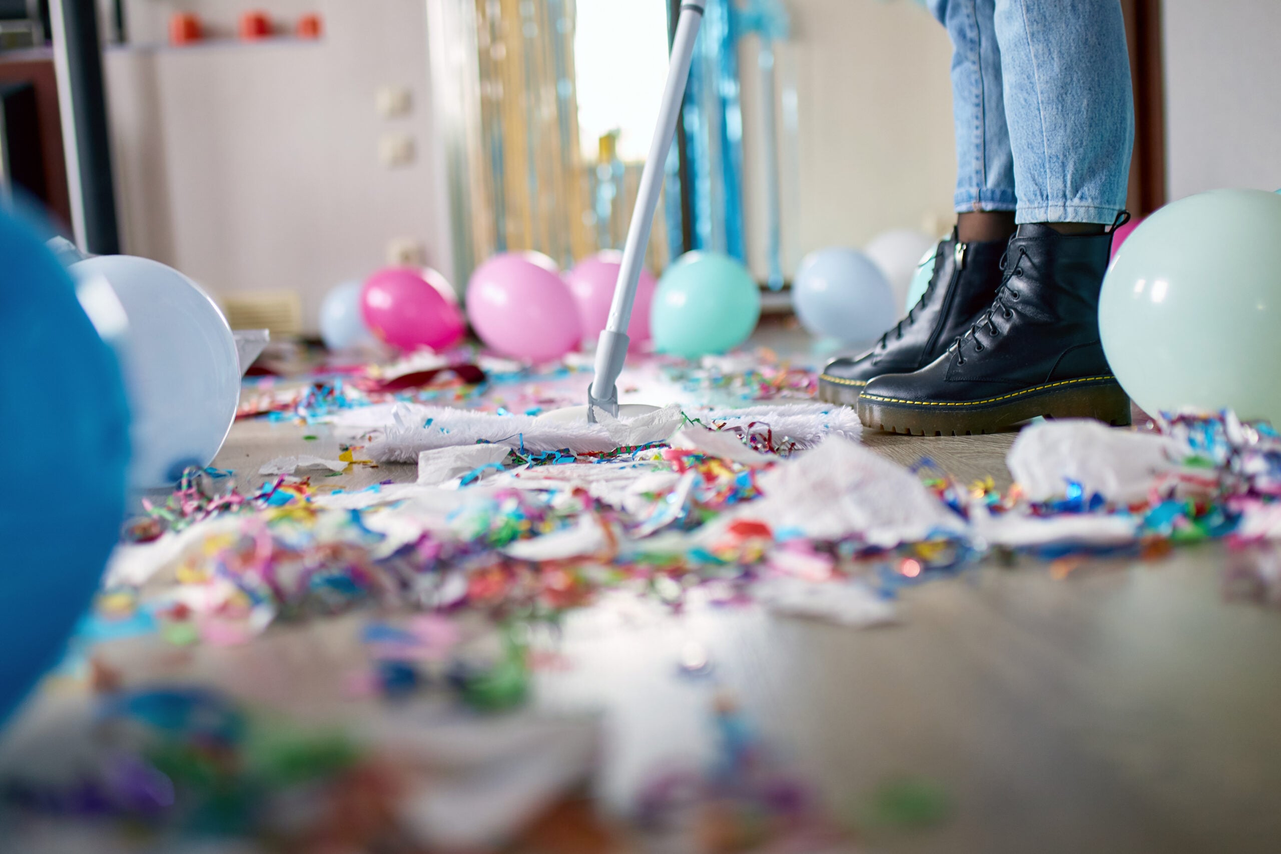 Woman with pushbroom cleaning mess of floor in room after party.