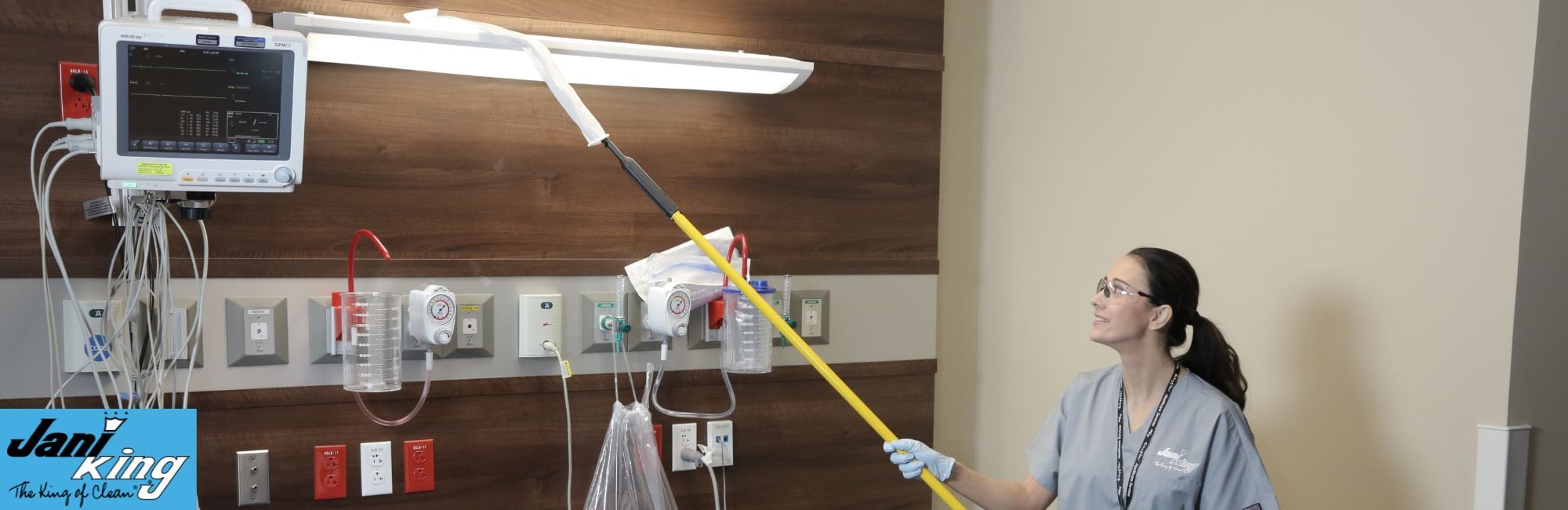 Jani-King employee cleaning a overhead light in a hospital room.